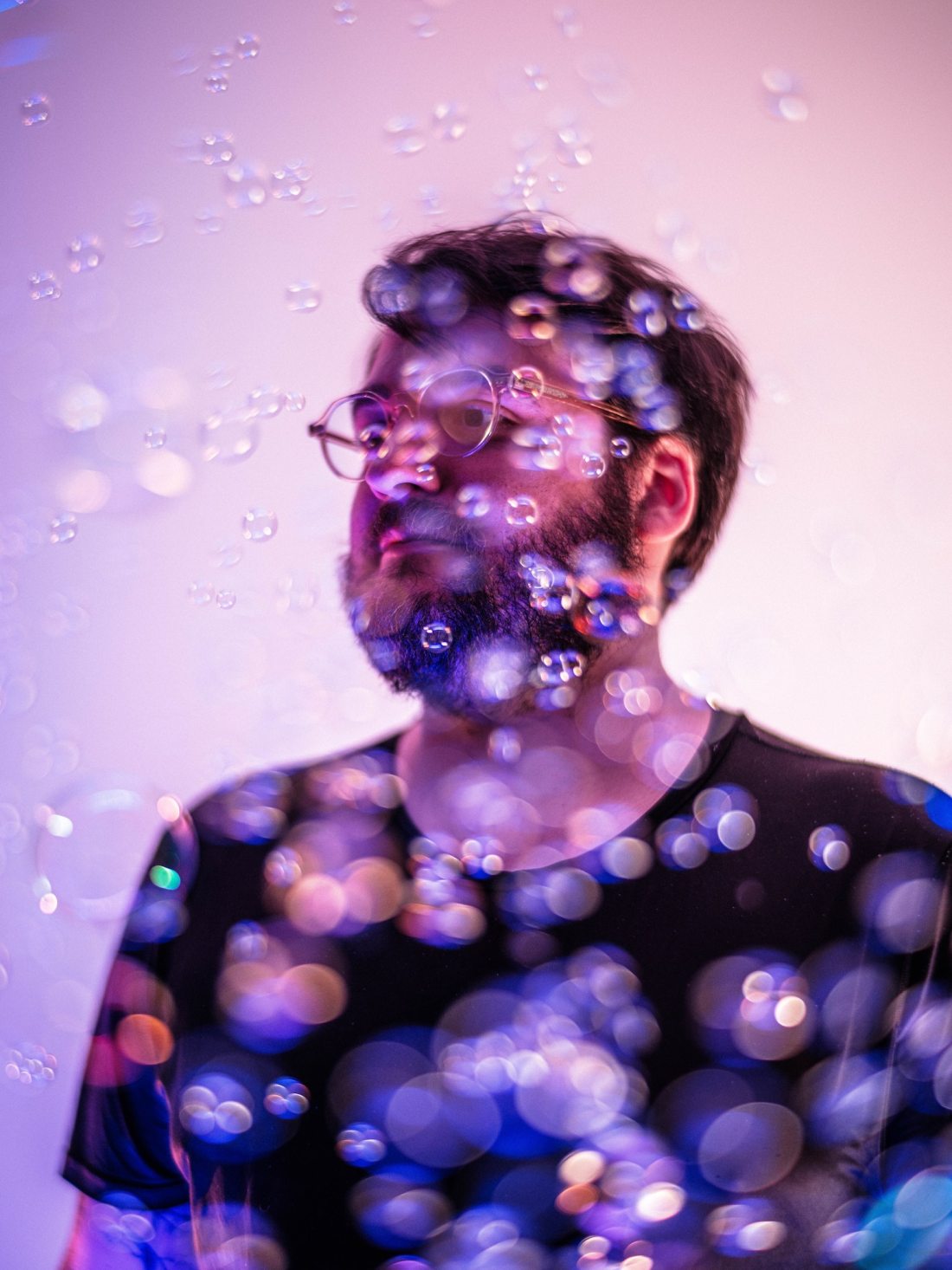 Self-portrait of Daniel Agee, a bearded man wearing glasses, surrounded by bubbles and with purple lighting.