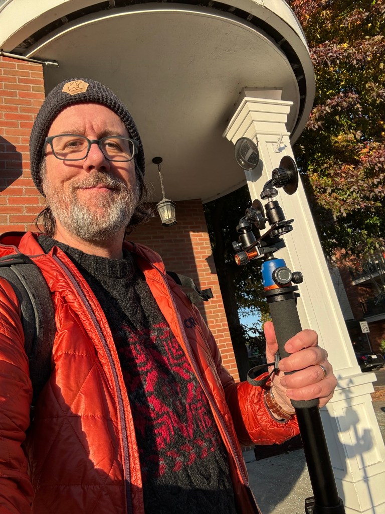 Smiling bearded man taking a selfie and holding a monopod.