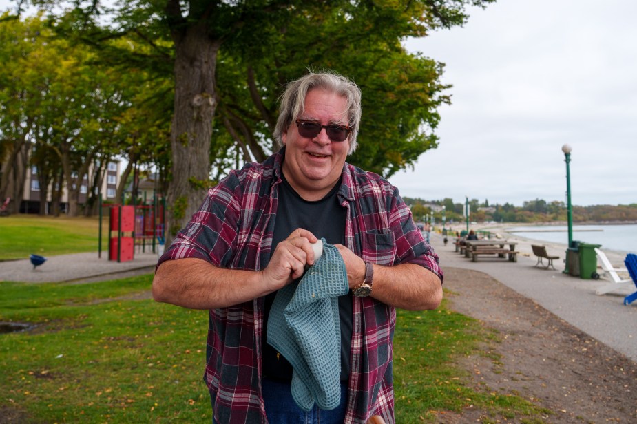 A smiling man in a park, cleaning a small espresso cup with a towel.