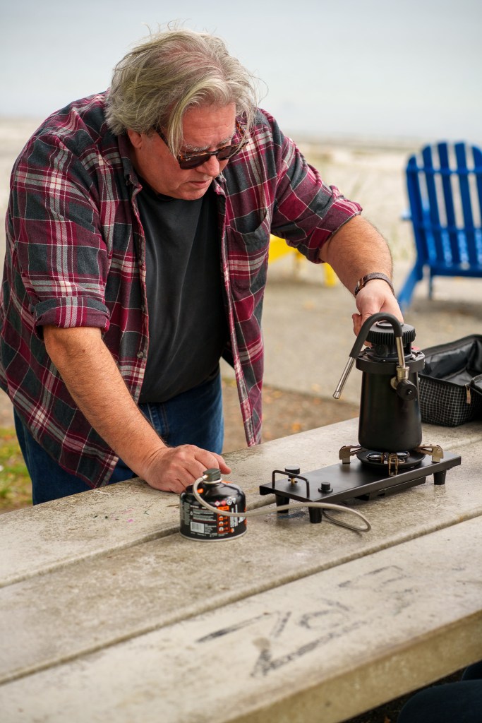 A man sets up a portable milk steamer on a park bench.