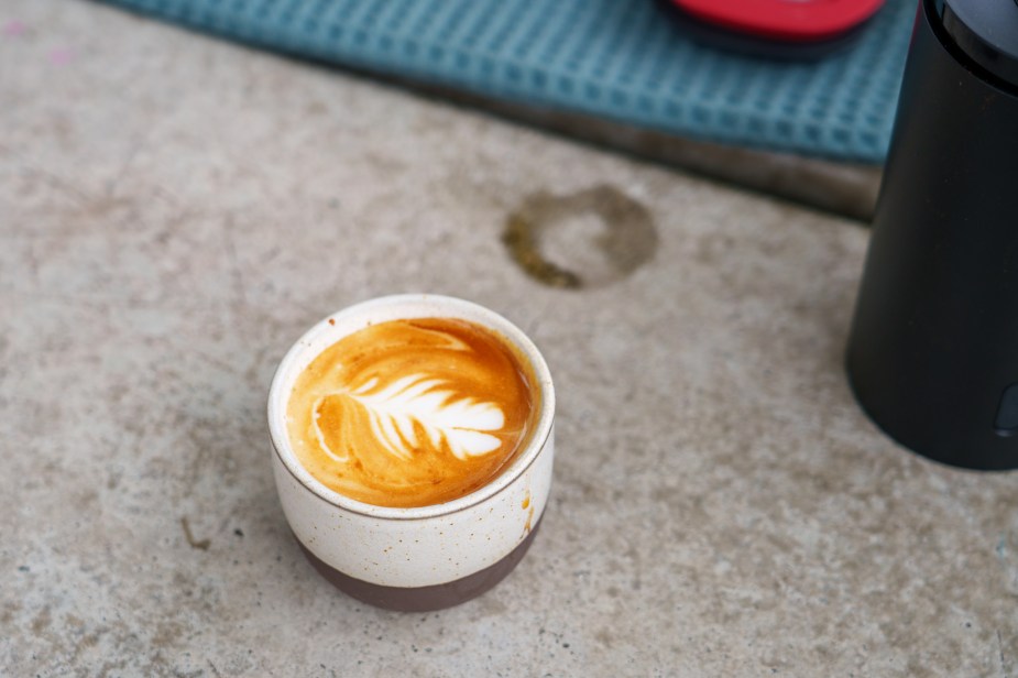 A small espresso cup with a cortado milk drink. It has a flower latte art pattern.