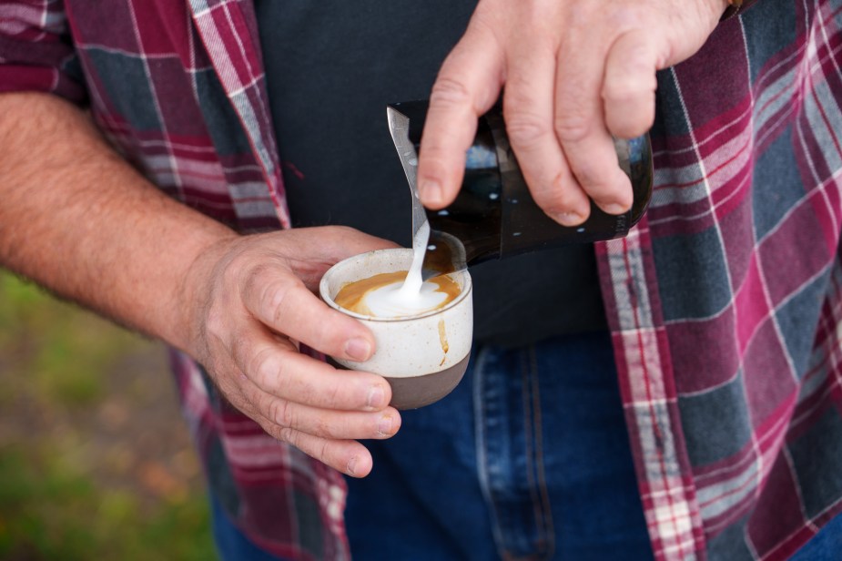 Closeup of a man pouring milk into a small coffee cup.
