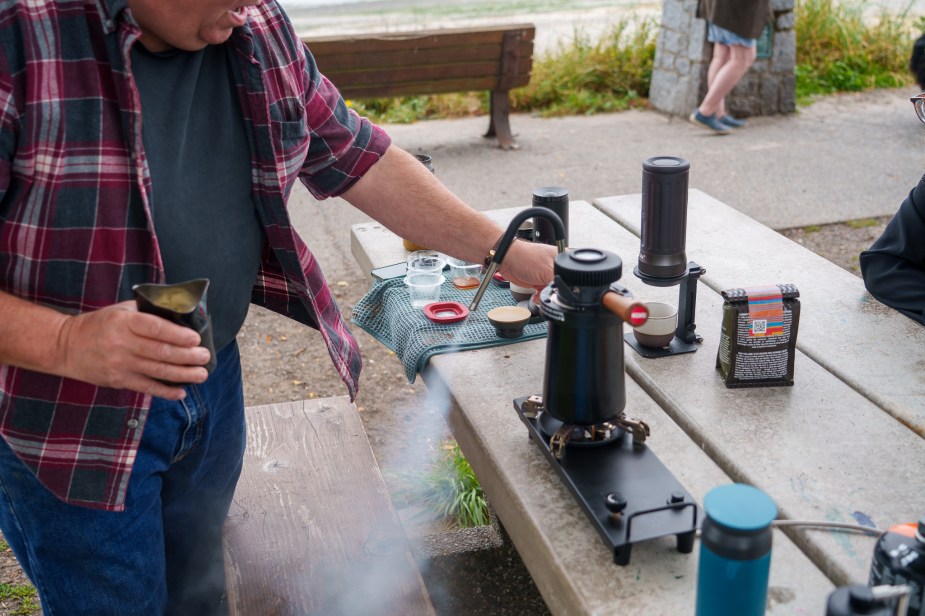 A man releases steam from a portable milk steamer that's sitting on a park bench.